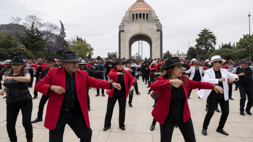 Multitud caracterizada con sombreros y chaquetas rojas bailando en la explanada del Monumento a la Revolución.